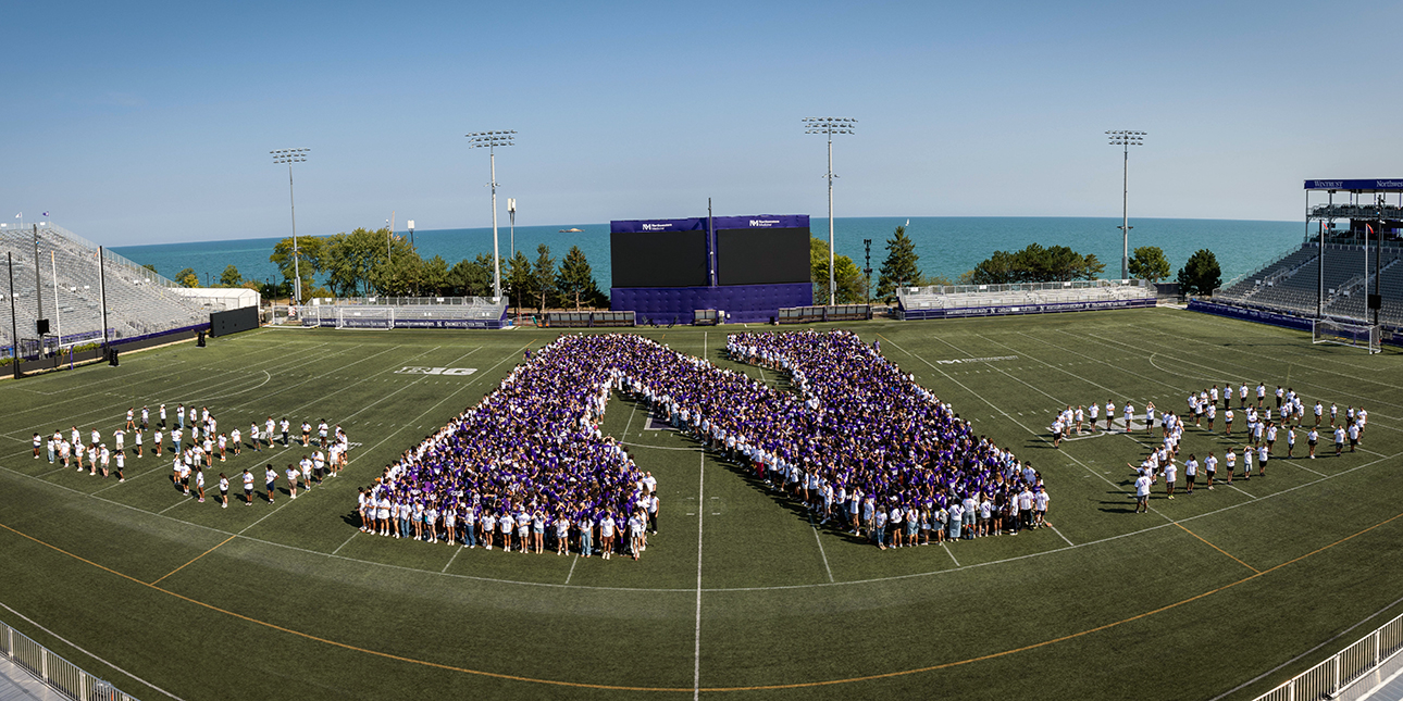 An aerial view of students from the Class of 2028 on a football field, where the students are arranged to form a giant purple N as well as the number 2028.