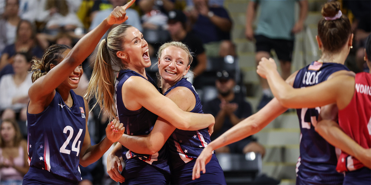 LOVB Pro players Annie Drews and Jordyn Poulter hug in celebration on the court, while teammate Chiaka Ogbogu points and smiles at their teammates in the foreground.