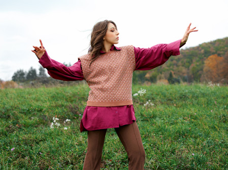 Anne-Sophie Lacombe García stands in a field of grass, wearing high heels, with her arms outstretched as she faces her head to the right.
