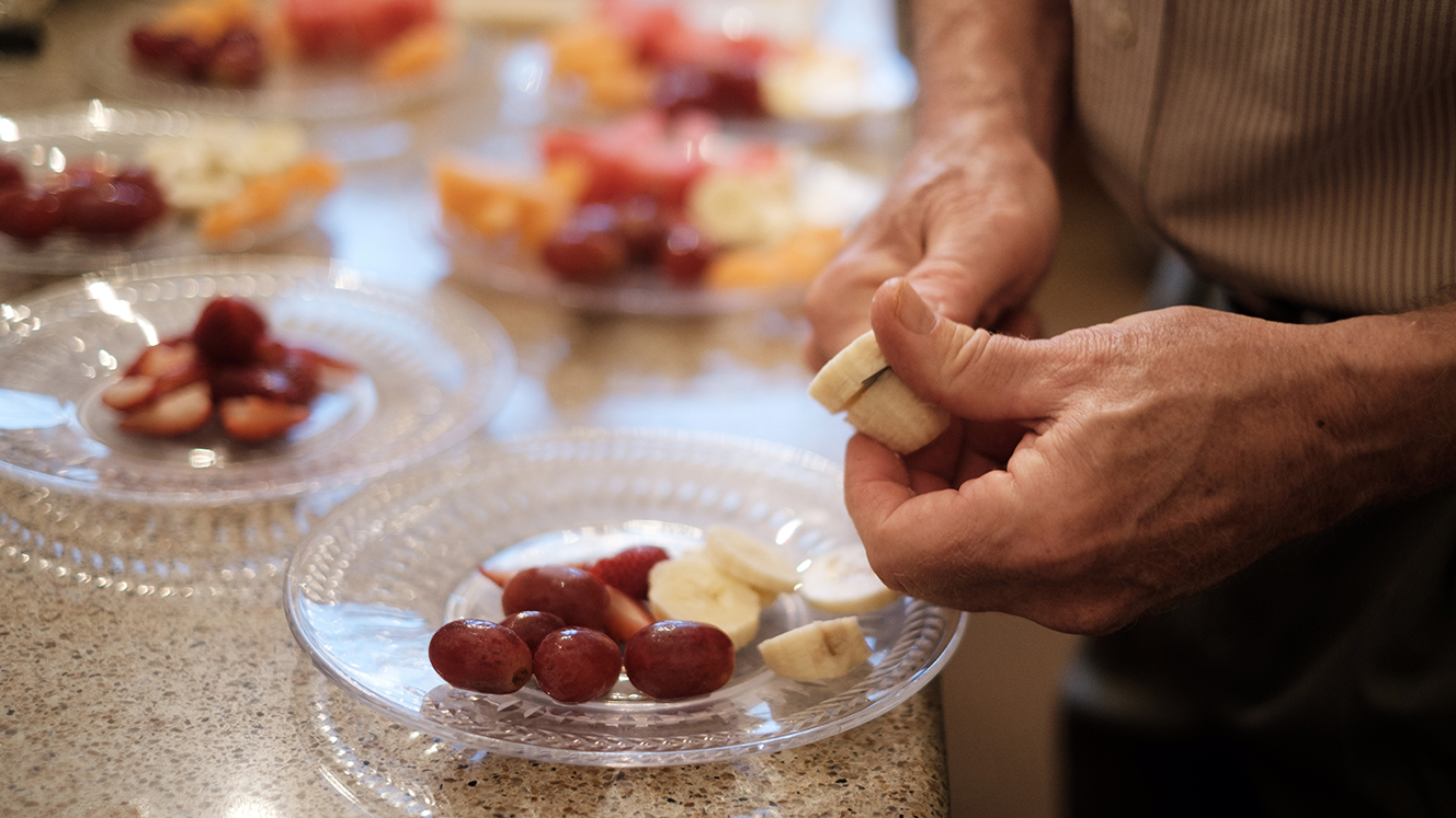 A close-up of Scott’s hands as he slices fruit. There are plates nearby with assorted pieces of fruit on them. 