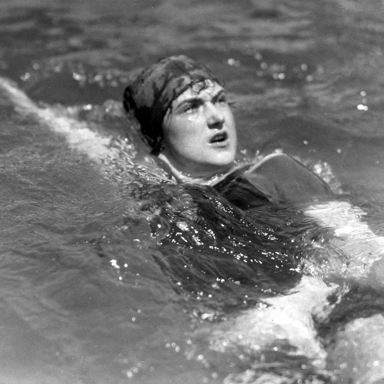 A black-and-white photo of Sybil Bauer swimming the backstroke while wearing a swimming cap.
