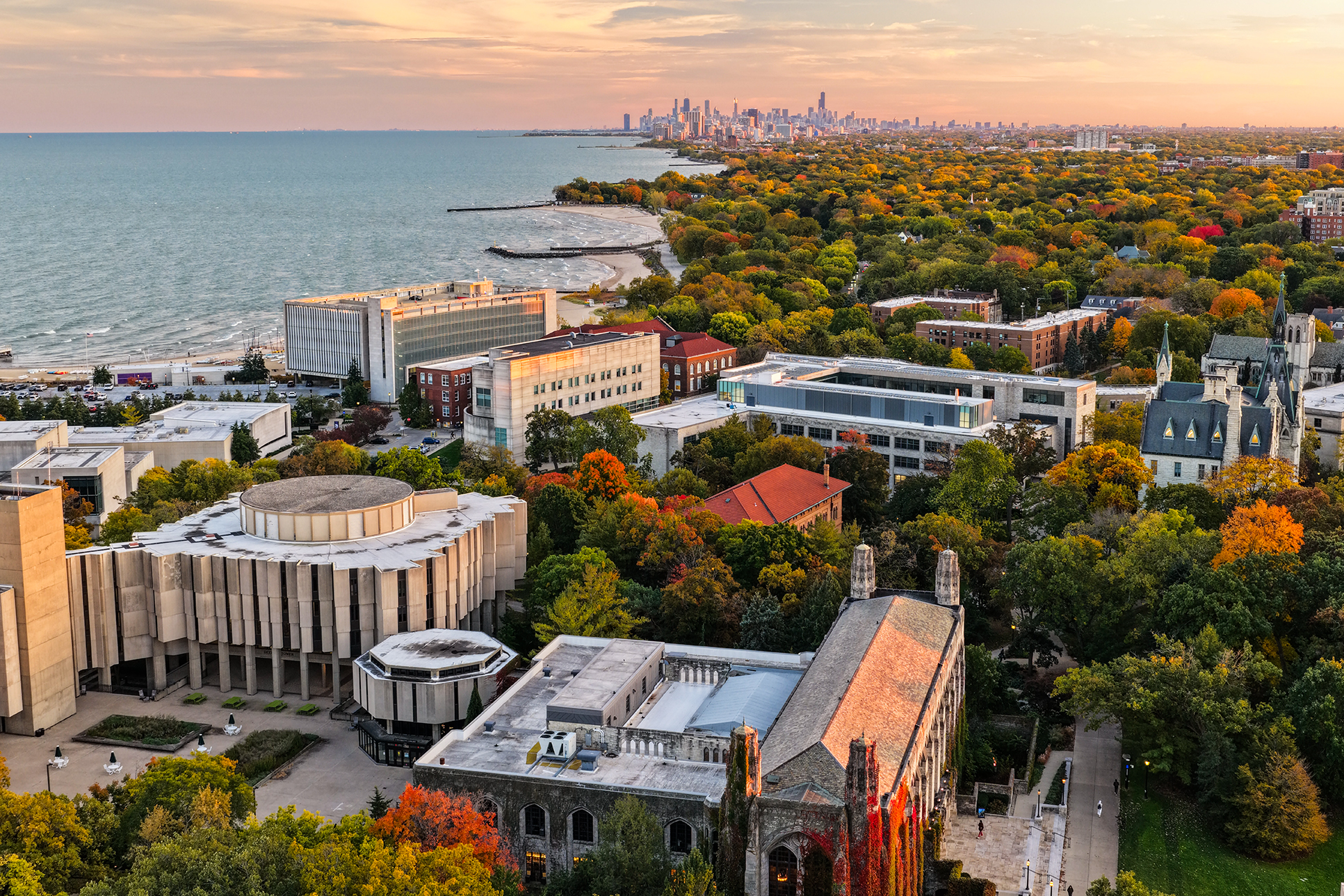 An aerial shot of Northwestern’s campus in the fall, facing south. To the left is Lake Michigan, to the right is a cluster of autumn trees, and in the distance stands Chicago’s skyline.
