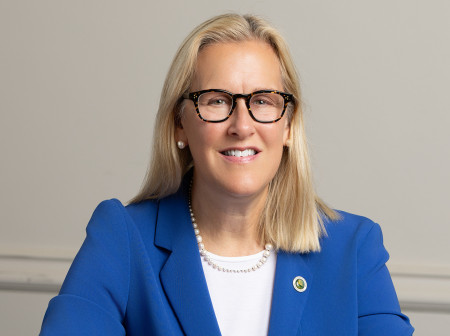 Mayor Nancy Rotering sits at a table wearing a blue jacket and smiling with her hands folded.