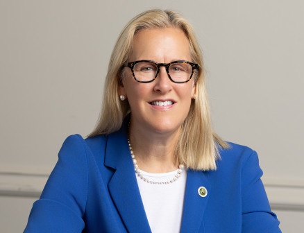 Mayor Nancy Rotering sits at a table wearing a blue jacket and smiling with her hands folded.