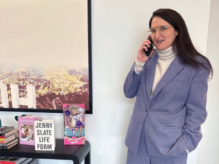 Shauna Perlman stands in a blue suit while talking on the phone next to a table filled with various books and a Northwestern Barbie.