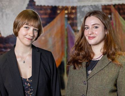 Two young women in blazers smile for the camera.