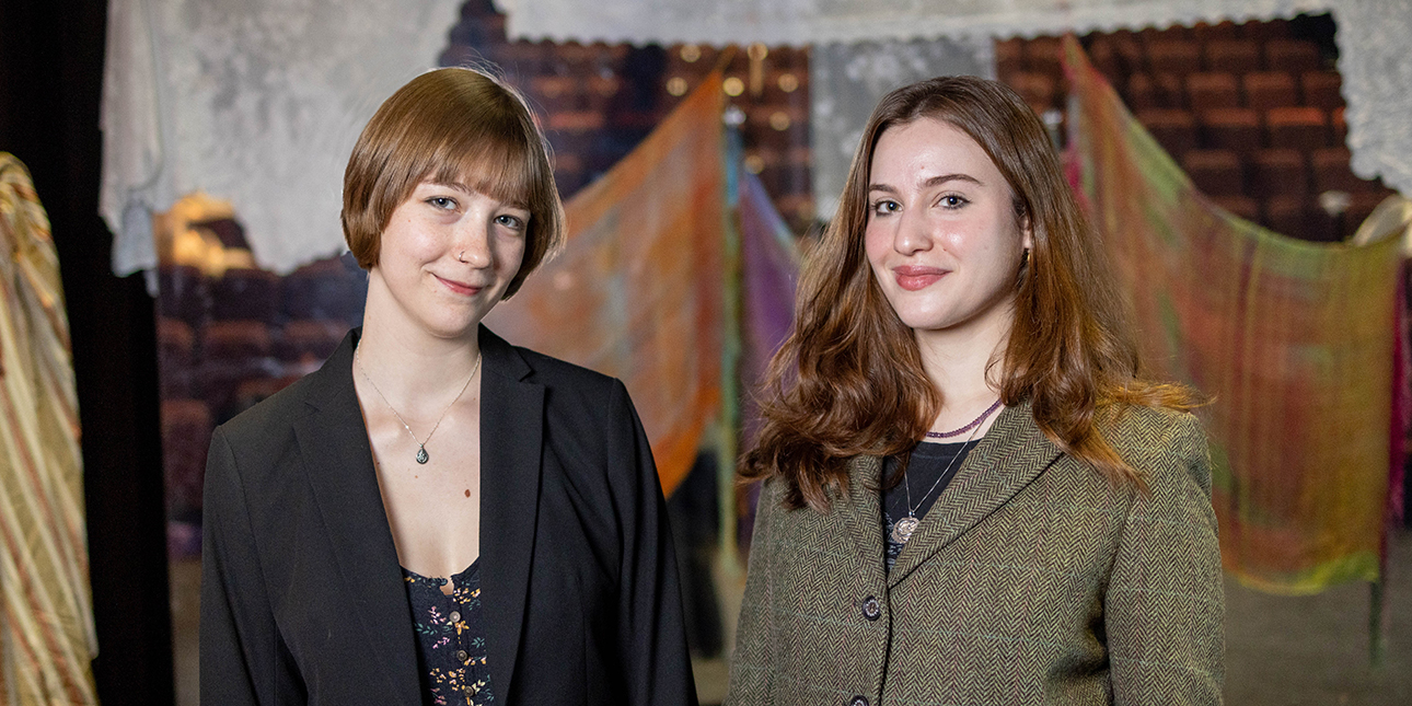 Two young women in blazers smile for the camera.