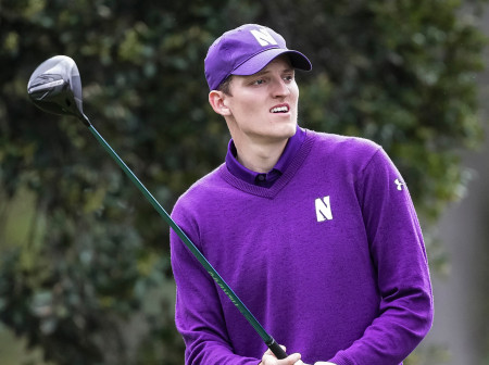 Daniel Svärd, dressed in a purple Northwestern hat, polo and sweater, holds his club up after finishing a swing and watches his shot.