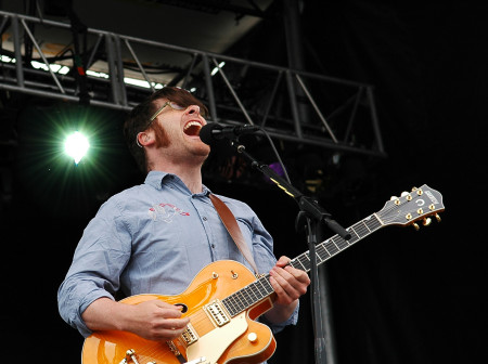 A man sings into the microphone and plays a guitar on stage.