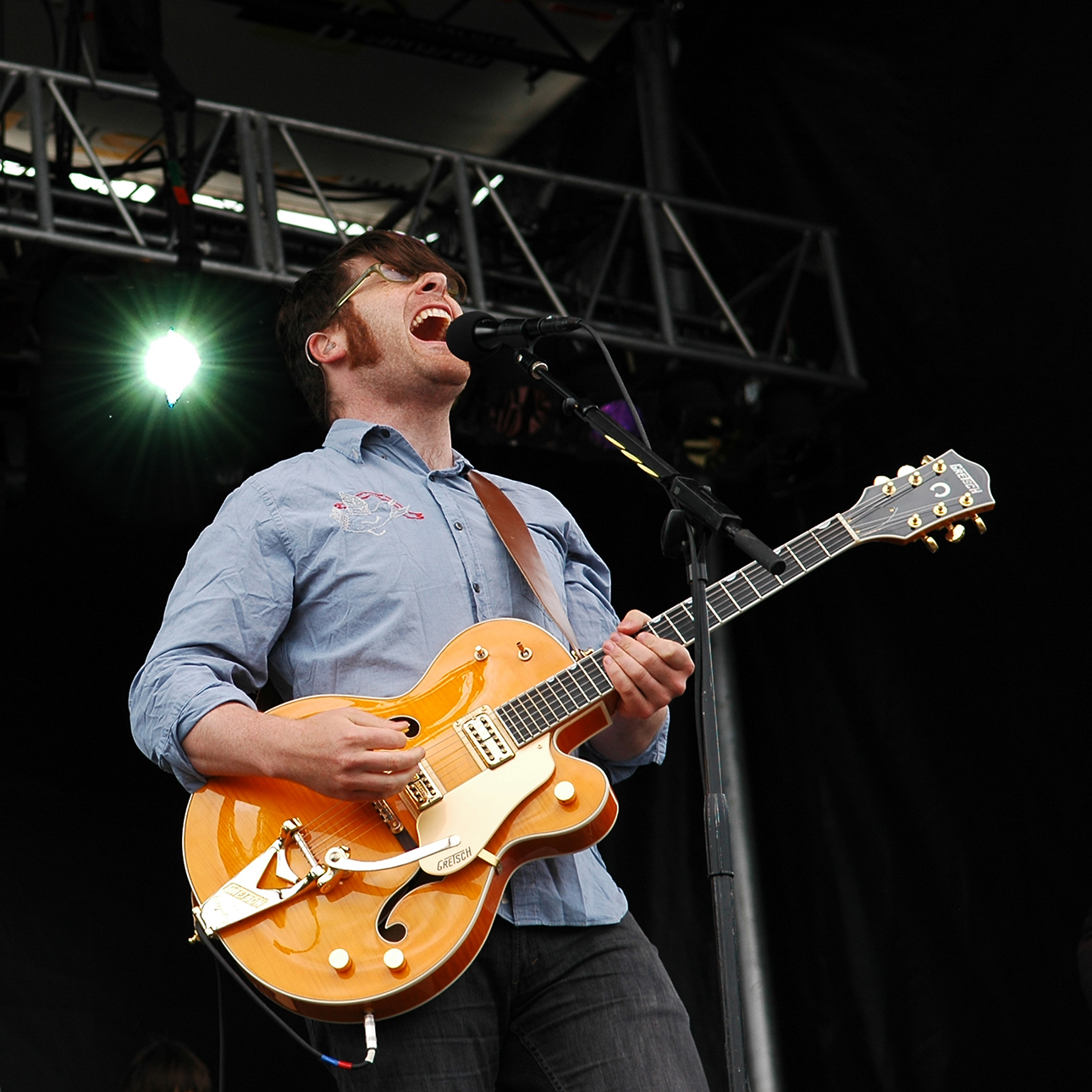 A man sings into the microphone and plays a guitar on stage.