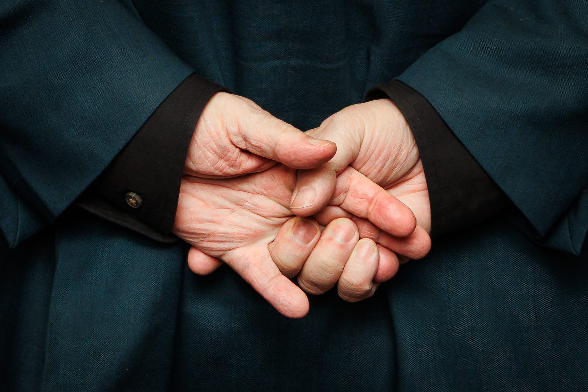 Two hands clasped behind the back of a person in a suit.
