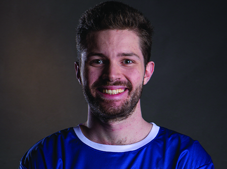 Jake Lyons smiles for a headshot in a blue t shirt