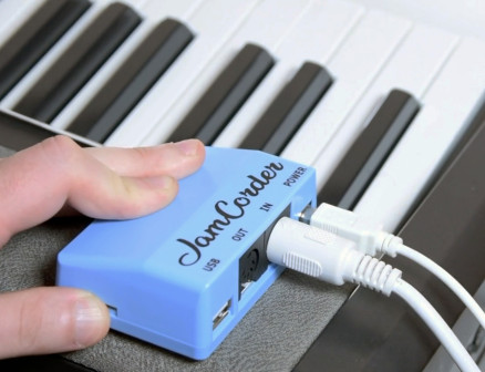 JamCorder, a small blue rectangular device, is hooked up to two wires and rests atop a keyboard.