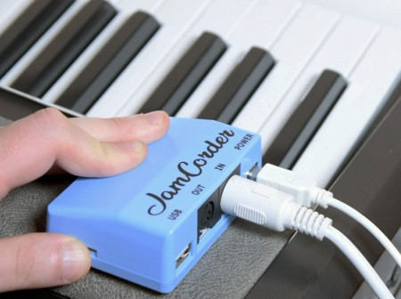 JamCorder, a small blue rectangular device, is hooked up to two wires and rests atop a keyboard.
