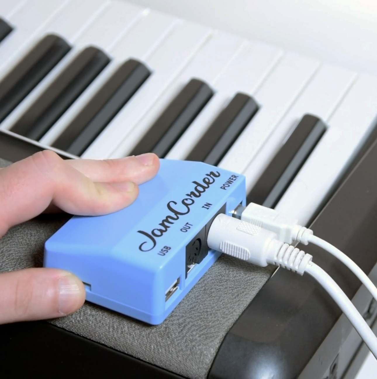 JamCorder, a small blue rectangular device, is hooked up to two wires and rests atop a keyboard.