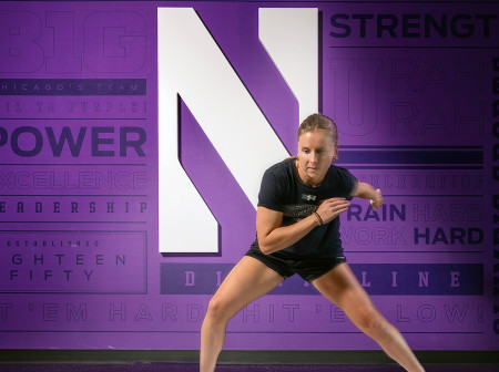A young woman uses the UltraSlide, pushing off one side to glide to the other, against a purple Northwestern background.