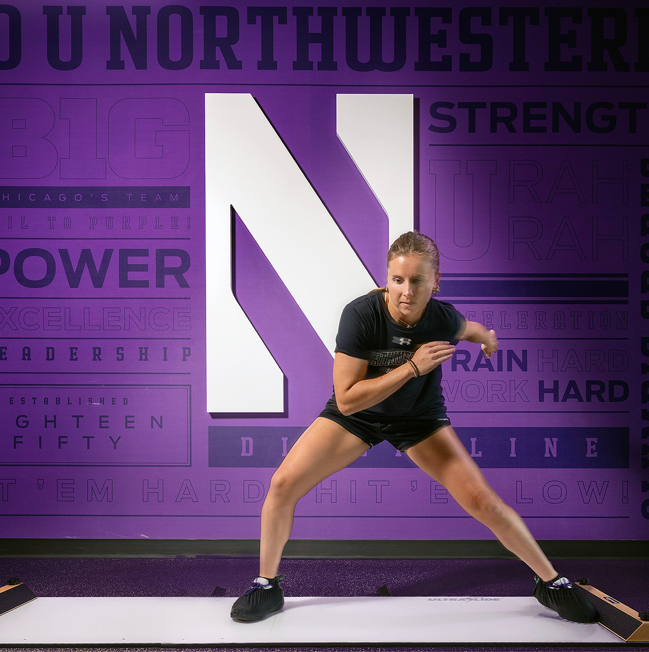 A young woman uses the UltraSlide, pushing off one side to glide to the other, against a purple Northwestern background.