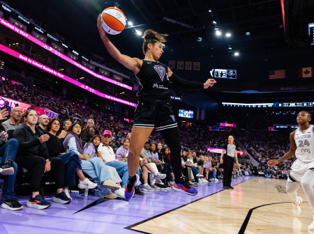 Veronica Burton leaps in the air, basketball in one hand with a defender opposite her.