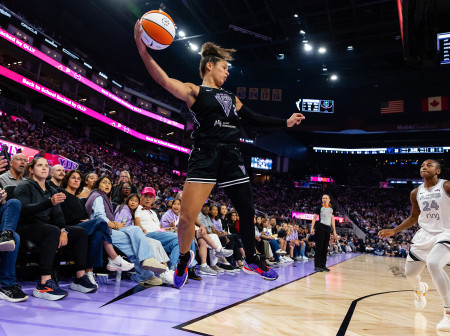 Veronica Burton leaps in the air, basketball in one hand with a defender opposite her.