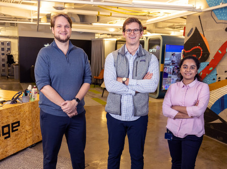 Two men and a woman stand in an industrial space looking at the camera and smiling.  