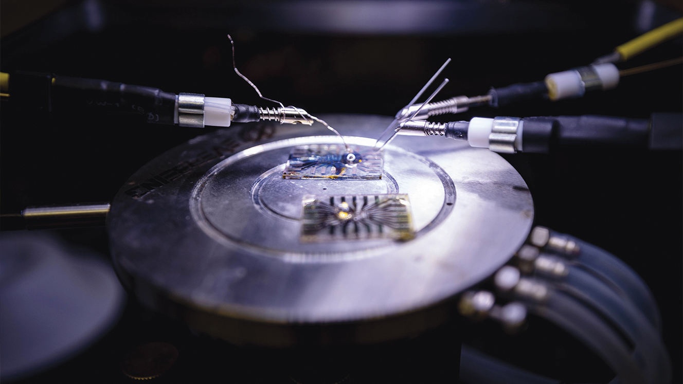  Small electronics lie flat on a metal disk while two robotic arms poke at them with metal pieces.