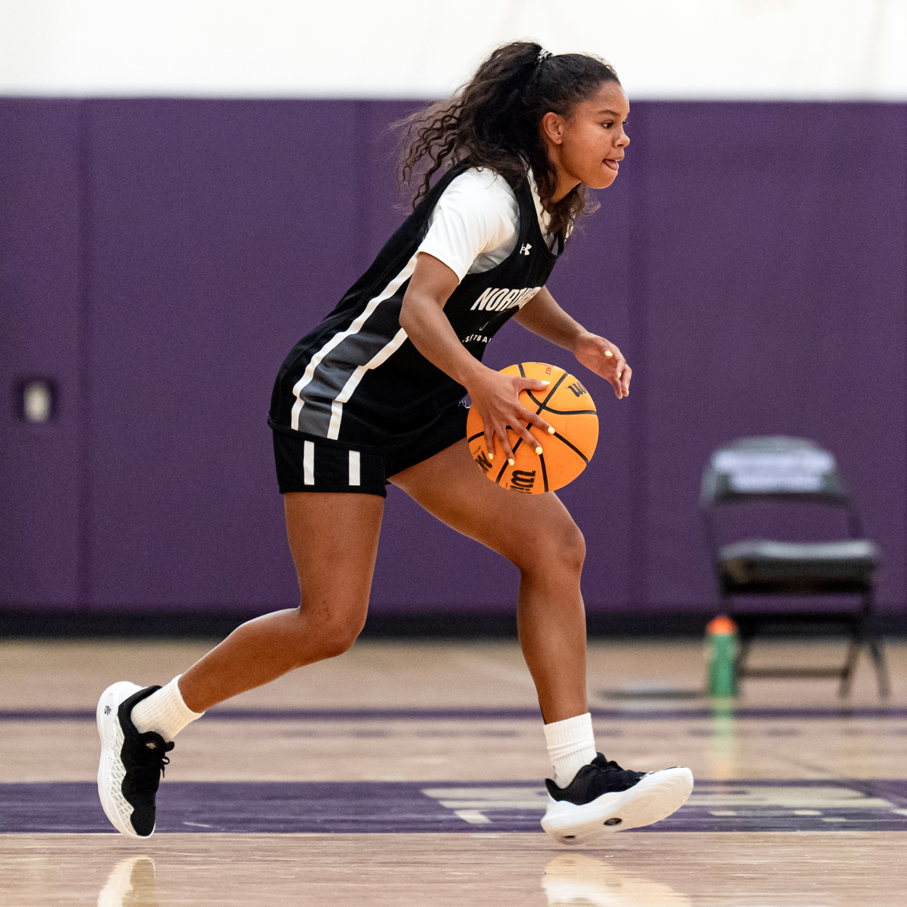 An action shot of Sammy White, wearing a Northwestern basketball uniform, palming a basketball.