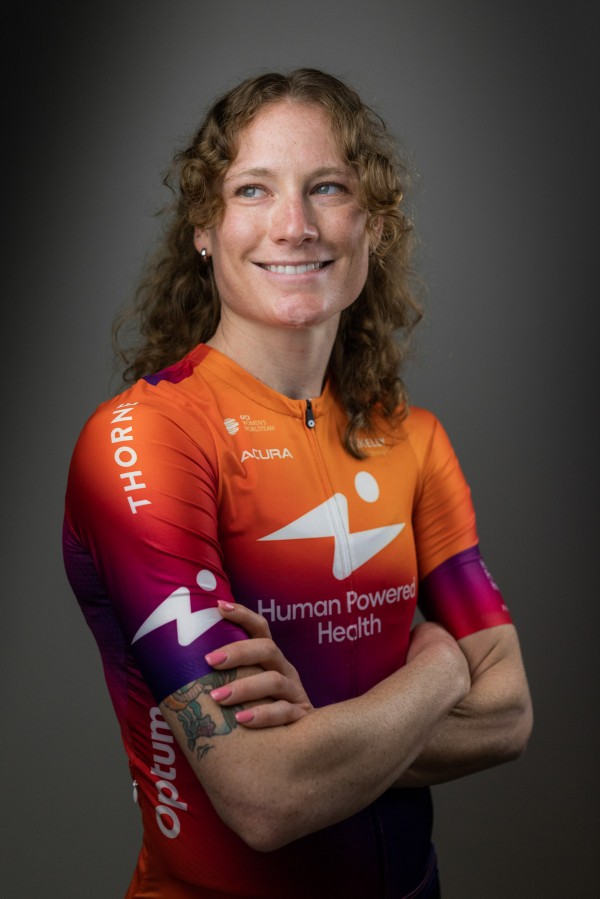 Lily Williams portrait from the waist up. She crosses her arms and wears an orange and red sport shirt. Her hair is down on her shoulders and she smiles off-camera.