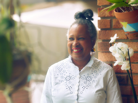 Monique Clesca leans up against a wall in Miami. She is smiling and wearing a white blouse. Her hair is in a bun.